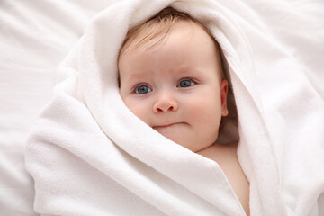 Cute little baby with soft towel lying on bed after bath, closeup