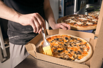 The cook greases the pizza with sauce.