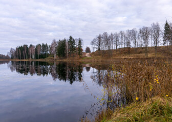 Opposite bank of lake in the autumn, cloudy sky, late autumn, bare tree silhouettes and reflections in the water