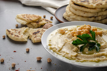Hummus in clay dish topped with chickpeas and green coriander leaves on stone table served with...
