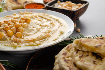 Low angle view at Hummus topped with chickpeas, olive oil and green coriander leaves on stone table with pita bread and spices aside