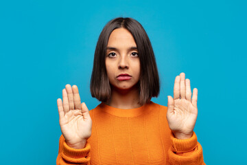 hispanic woman looking serious, unhappy, angry and displeased forbidding entry or saying stop with both open palms