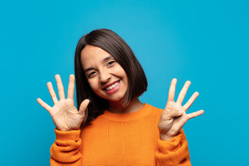 hispanic woman smiling and looking friendly, showing number nine or ninth with hand forward,...