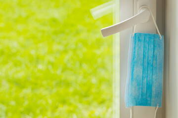 Mask hanging on the balcony door handle. Green grass outside the window. The concept of closing in...