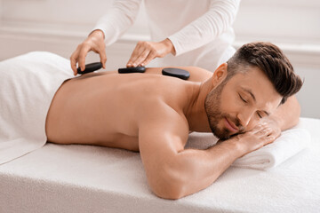 Joyful man having hot stone massage at luxury spa