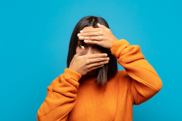 hispanic woman covering face with both hands saying no to the camera! refusing pictures or...