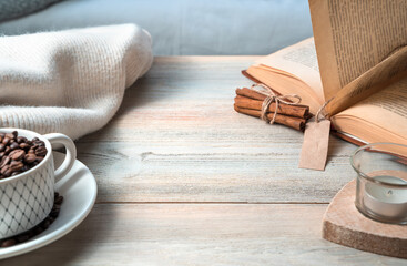 Fototapeta na wymiar Cozy background with a white Cup, sweater, book, coffee beans on a light wooden table. Side view.