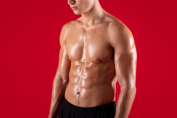 Closeup view of young strong sportsman with naked torso and prominent abs muscles on red studio background