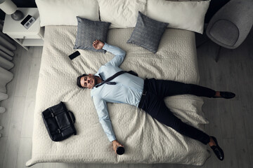 Exhausted businessman in office wear sleeping on bed at home after work, above view