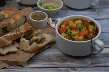 Potato, carrot and lima beans soup in white bowls on wooden backround, served with herb bread