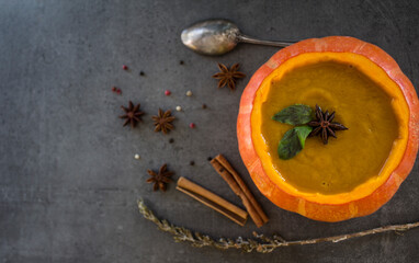 Spicy squash soup in pumpkin bowl. Top view photo on grey table. Winter receipts. 