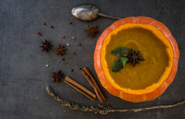 Spicy squash soup in pumpkin bowl. Top view photo on grey table. Winter receipts. 