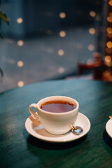 A cup of tea on a green wooden table, background from the back of Christmas lights