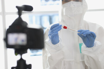 Doctor in protective suit and mask shows test tube and pay with test to the camera. Coronovirus...