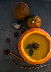 Squash soup in pumpkin bowl. Top view photo of pumpkin, apples, carrots anise stars and cinnamon sticks. Grey background. Autumn food close up photo. 
