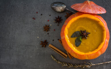 Spicy squash soup in pumpkin bowl. Top view photo on grey table. Winter receipts. 