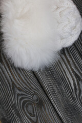Winter knitted hat with fur. White. Lies on black pine boards.