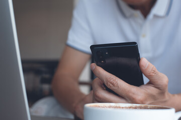 Man using mobile phone during online working on laptop computer in coffee shop