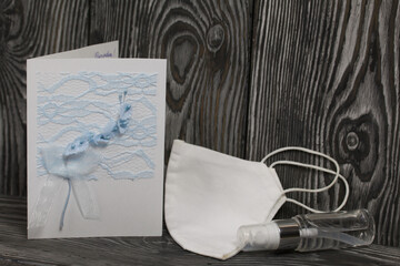 Greeting card, medical mask and antiseptic. They lie on black pine boards.
