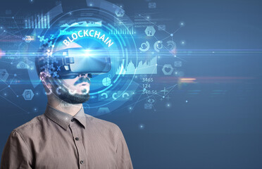Businessman looking through Virtual Reality glasses with BLOCKCHAIN inscription, innovative technology concept