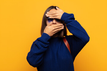 hispanic woman covering face with both hands saying no to the camera! refusing pictures or...