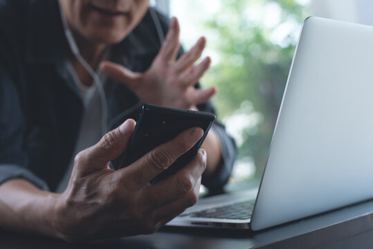 Man making facetime video call and discussion using zoom online meeting app via mobile phone, working on laptop computer from home office