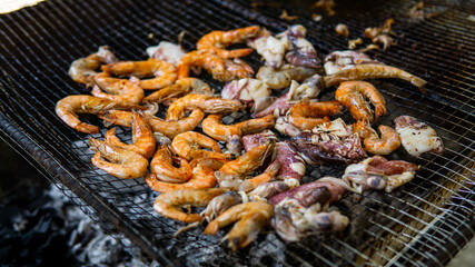 Close up view of grilled prawns and squids on the hot grill during summer picnic. Roasted seafood menu on a charcoal stove. Selective focus.