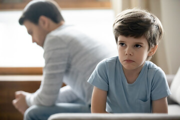 Close up upset little boy and father ignoring each other, not talking after quarrel, unhappy preschool son and dad sitting on couch separately, parent and child, family generations conflict