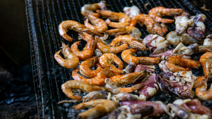 Close up view of grilled prawns and squids on the hot grill during summer picnic. Roasted seafood menu on a charcoal stove. Selective focus.