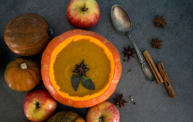 Squash soup in pumpkin bowl. Top view photo of pumpkin, apples, carrots anise stars and cinnamon sticks. Grey background. Autumn food close up photo. 

