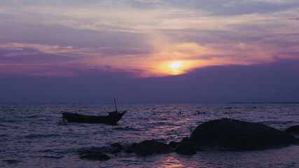 Silhouette of a fishing boat in the left of the picture, in the evening there is a sunset at the sea.