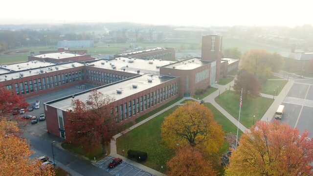 High angle aerial of school bus leaving large public school on foggy morning. Lancaster Pennsylvania USA.