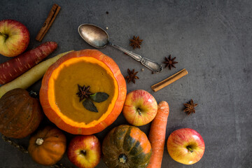 Squash soup in pumpkin bowl. Top view photo of pumpkin, apples, carrots anise stars and cinnamon sticks. Grey background. Autumn food close up photo. 

