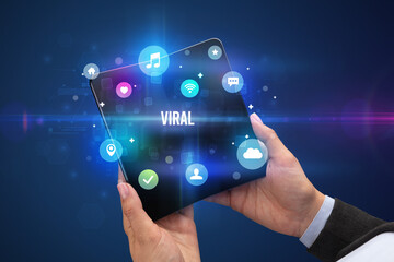 Businessman holding a foldable smartphone with VIRAL inscription, social media concept