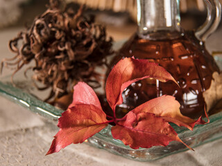 Close up of red leaf on a glass bowl on a background of a glass jug and brown hazelnuts