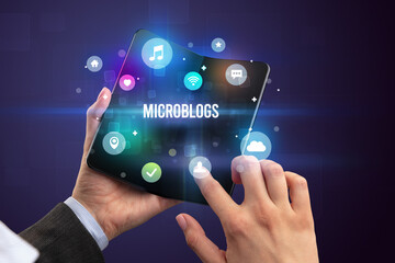Businessman holding a foldable smartphone with MICROBLOGS inscription, social media concept