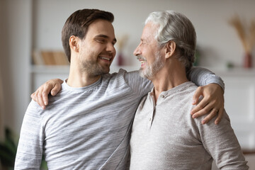 Close up overjoyed mature father with adult son hugging, excited older grandfather and grown up grandchild having fun, chatting, family enjoying leisure time together, two generations bonding - obrazy, fototapety, plakaty