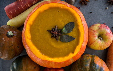 Squash soup in pumpkin bowl. Top view photo of pumpkin, apples, carrots anise stars and cinnamon sticks. Grey background. Autumn food close up photo. 
