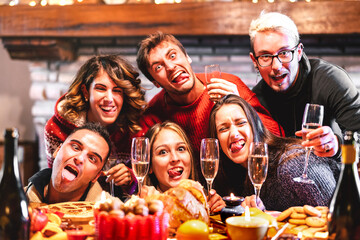 Happy friends taking crazy drunk selfie celebrating Christmas time with champagne and sweets food at dinner reunion party - Winter holiday concept with people having fun eating together - Warm filter