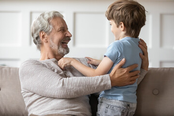 Close up overjoyed grandfather hugging adorable grandson, two generations having fun at home...