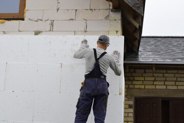 Worker installing white rigid polyurethane foam sheet on building wall facade for energy saving....