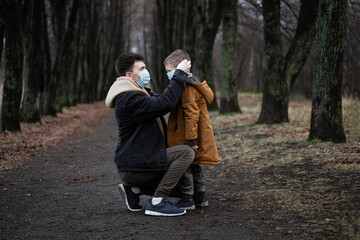 dad puts a medical mask on his little son, young dad walks in the park with his son, winter park, autumn truancy