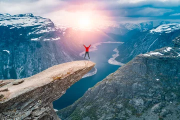 Tragetasche Norwegen, eine Frau, die auf der Klippe der Berge von Trolltunga thront, die über Ringedalsvatnet thront und den Sonnenuntergang und die schneebedeckten norwegischen Berge in der Nähe von Odda, Rogaland, Norwegen beobachtet © Dmitry Pistrov