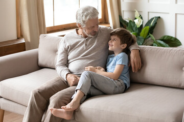 Mature grandfather talking with adorable grandson, sitting on couch, loving old man and little boy grandchild enjoying leisure time, tender moment, having pleasant conversation, two generations