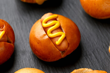 Mini hot dogs with yellow mustard on black slate board
