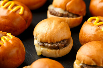 Mini hamburgers, burger and hot dogs with yellow mustard on black slate board