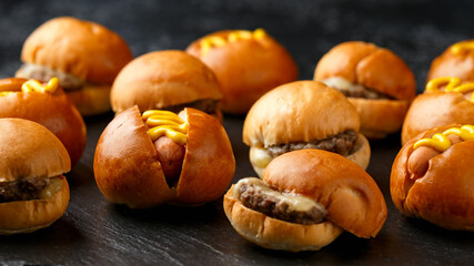 Mini hamburgers, burger and hot dogs with yellow mustard on black slate board