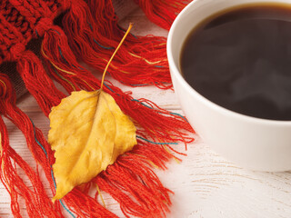 Close-up of dry yellow fall leaf on a knitted red fringed scarf near white mug of hot steaming...