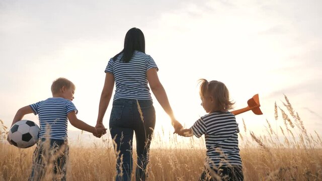 Happy family mom son and daughter walks in the park at sunset. Friendly family play ball and plane together. Parent plays with son and daughter in toys in the park outdoors