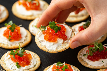 Salmon caviar and soft cheese savory crackers with sesame and poppy seeds served on black slate board